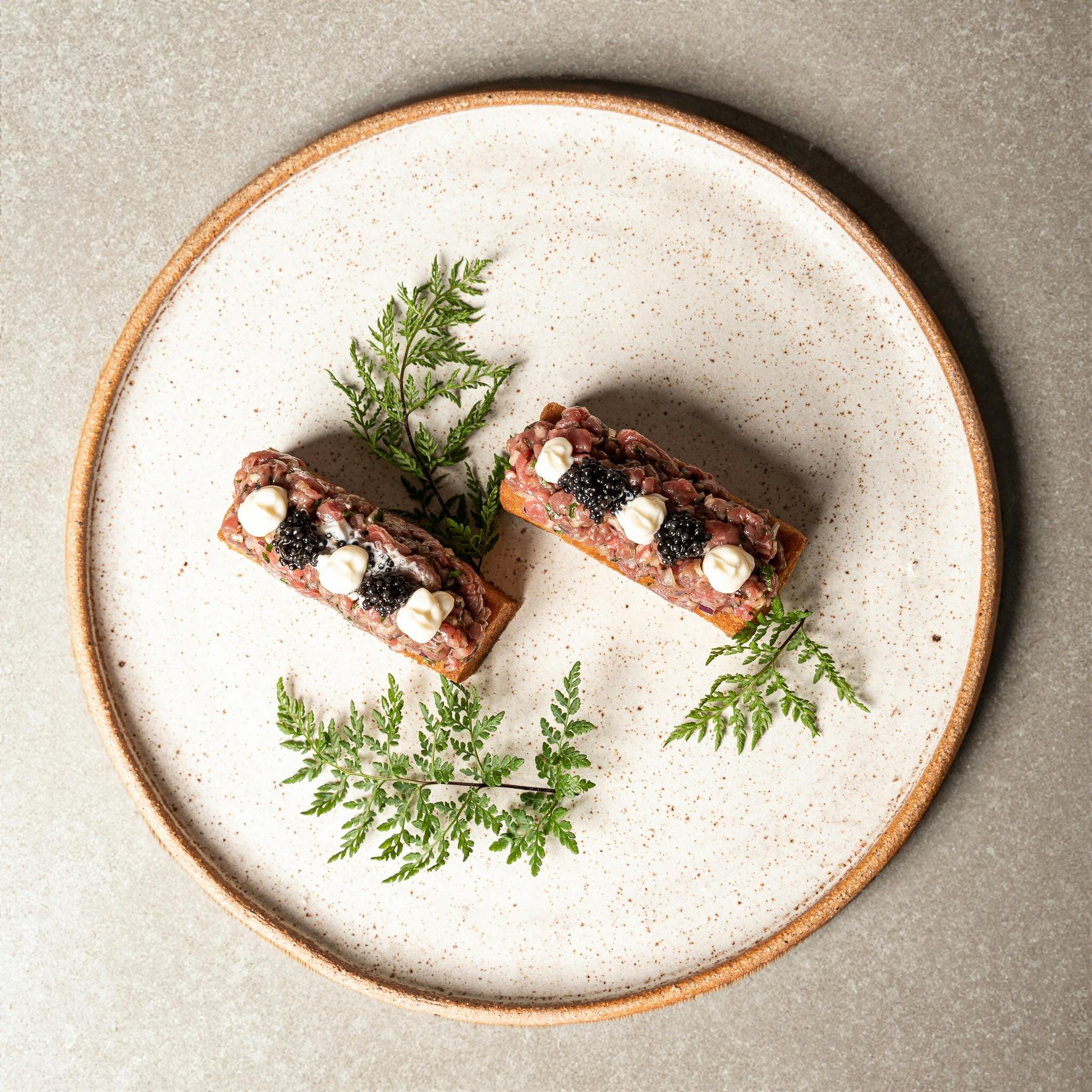 Caviar tapas pairing on a stylish plate featuring creative tapas bites with caviar pearls, decorated with ferns, perfect for elegant dining and events.