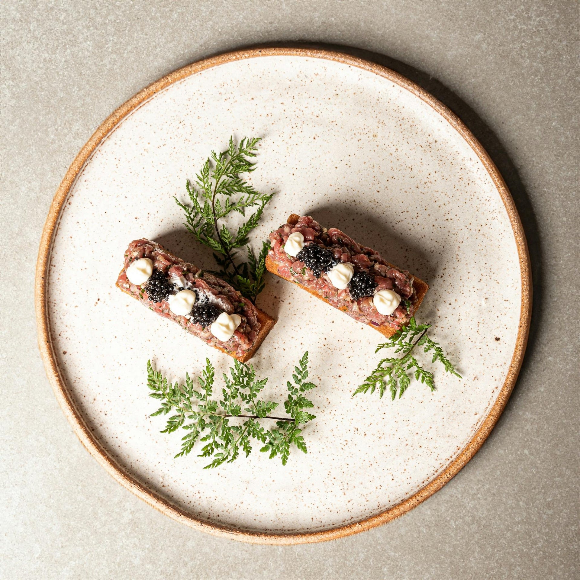 Caviar tapas pairing on a stylish plate featuring creative tapas bites with caviar pearls, decorated with ferns, perfect for elegant dining and events.